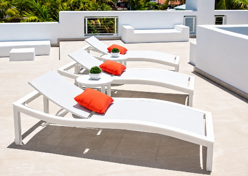 Modern curved chaise lounges with white frames and accent pillows creating a sophisticated luxury pool deck design.